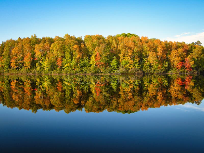 Lush fall colored trees reflection in blue lake water.