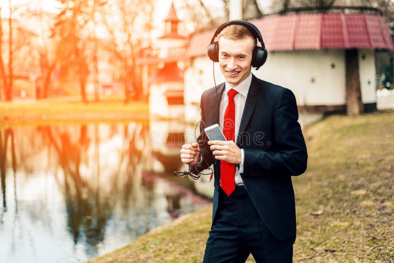 Lustiger junger Kerl hört Musik mit großen Kopfhörern ein Mann in einem schwarzen Anzug und in einer roten Bindung Geschäftsmanns lizenzfreies stockbild Lustiger junger Kerl hört Musik mit großen Kopfhörern ein Mann in einem schwarzen Anzug und in einer roten Bindung Geschäftsmanns lizenzfreies stockbild