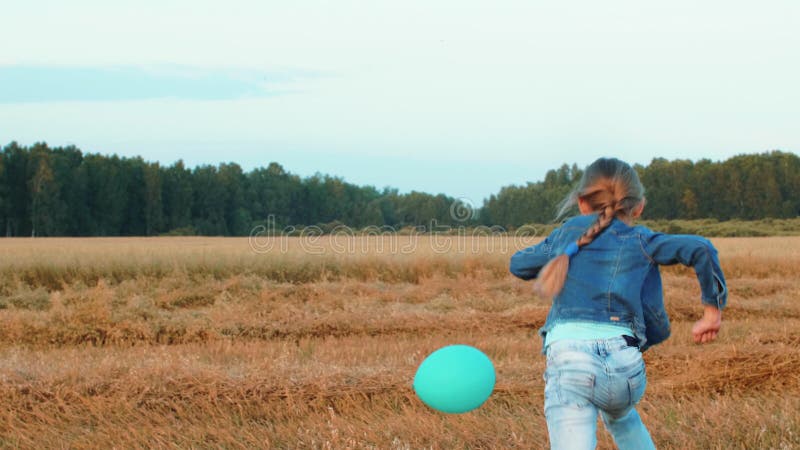 Lustiges Jugendlichmädchen, das mit Ballon auf Weizenfeld in der Landschaft spielt