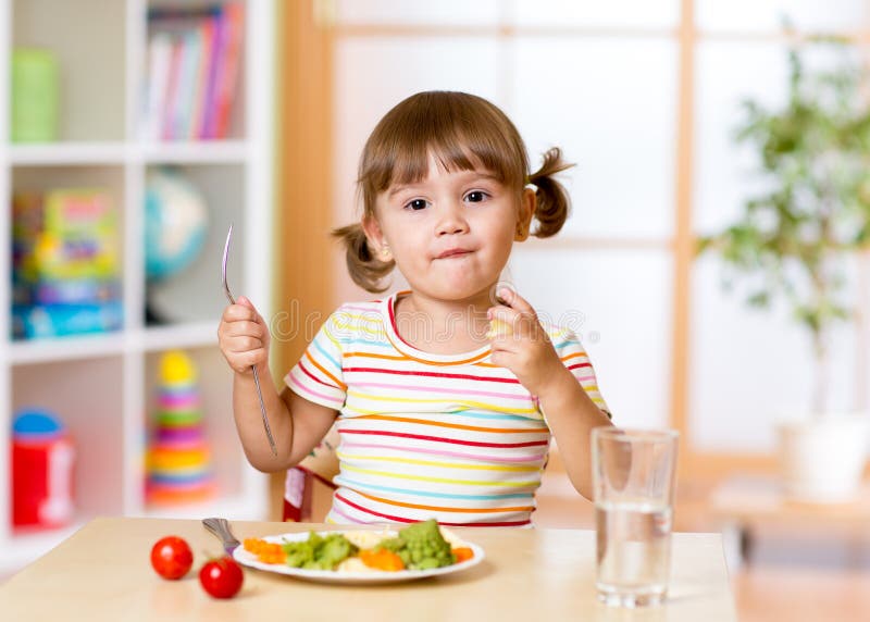 Lustiges kleines Mädchen isst im Kindergarten zu Abend lizenzfreie stockfotos Lustiges kleines Mädchen isst im Kindergarten zu Abend lizenzfreie stockfotos
