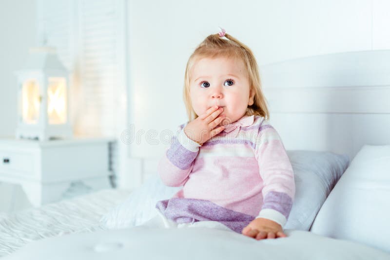 Lustiges überraschtes blondes kleines Mädchen, das auf Bett im Schlafzimmer sitzt lizenzfreie stockfotografie Lustiges überraschtes blondes kleines Mädchen, das auf Bett im Schlafzimmer sitzt lizenzfreie stockfotografie