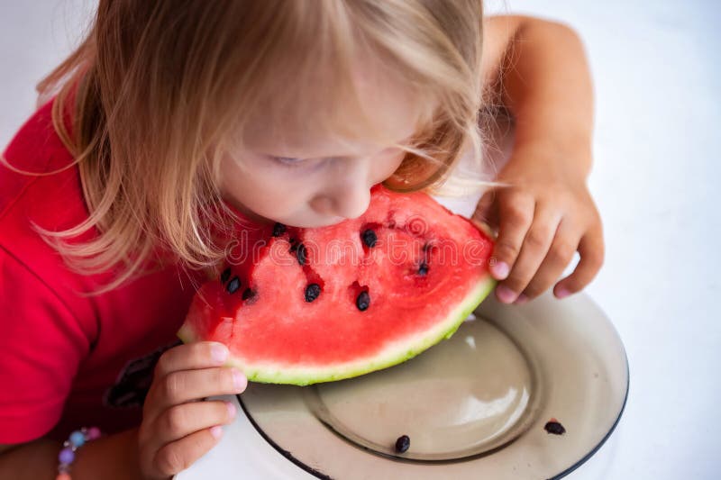 Lustigt, blond, underordnad porträtt med vattenmelon inomhus uppåt. Sötaste lilla småbarn 4 år som äter vattenmelonsoluppgång arkivbild