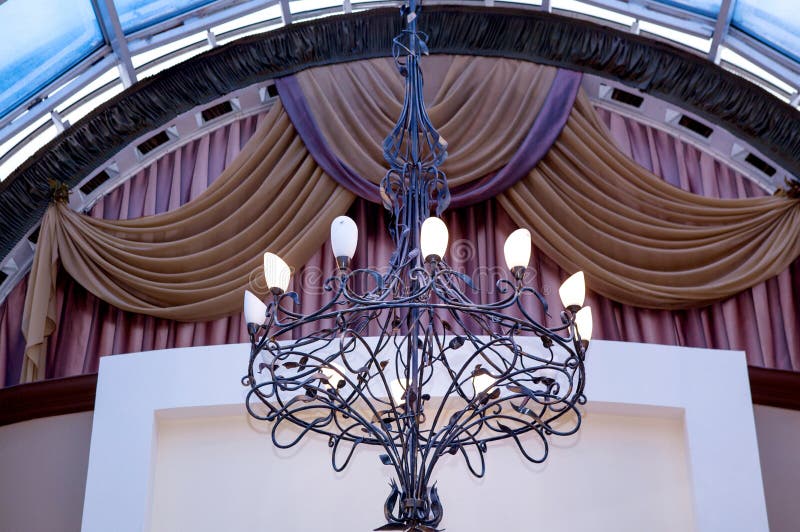 Lustre élégant de fer travaillé sur le plafond contre le contexte des rideaux image stock Lustre élégant de fer travaillé sur le plafond contre le contexte des rideaux image stock