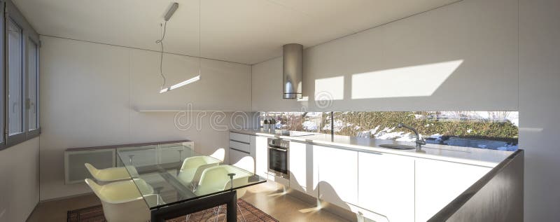 Luxurious kitchen with dining table and four chairs inside. A modern and stylized lamp hangs from the ceiling royalty free stock photography