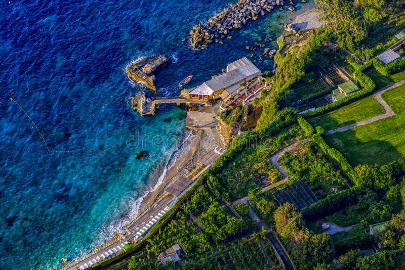 La costa rocciosa dell'isola di Capri con un brillante verde di giardini curati e una spiaggia di ghiaia.