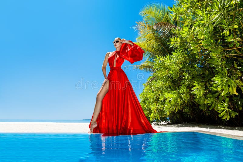 Luxury fashion. Elegant fashion model. Stylish female model in red long gown dress on the Maldives beach. Elegance. Classy woman