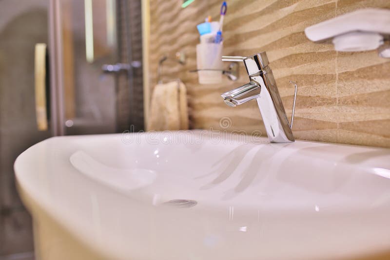 Luxury faucet mixer on a white sink in a beautiful gray interior bathroom. nice metal faucet in modern bathroom stock photo Luxury faucet mixer on a white sink in a beautiful gray interior bathroom. nice metal faucet in modern bathroom stock photo