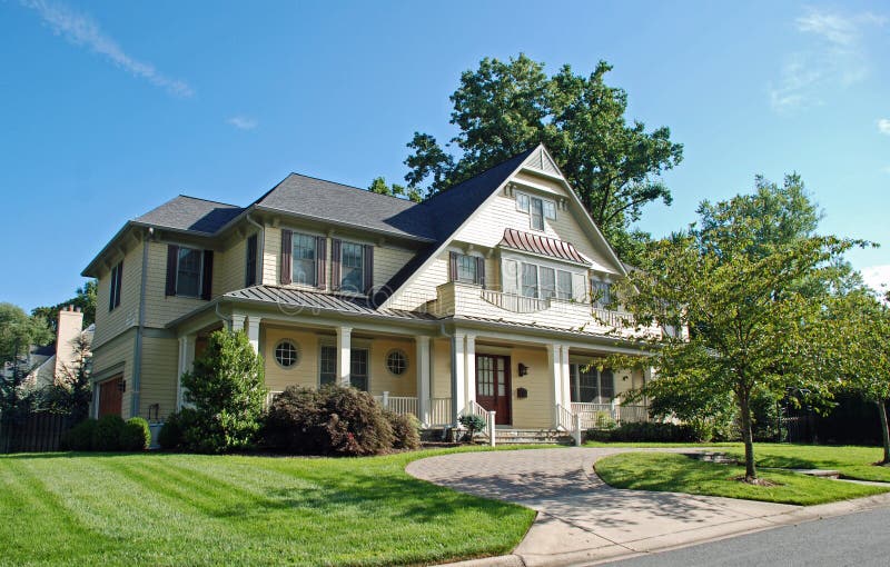 Large luxury home with yellow siding, perfect green grass lawn, and a driveway of brick and paving stone. Large luxury home with yellow siding, perfect green grass lawn, and a driveway of brick and paving stone.