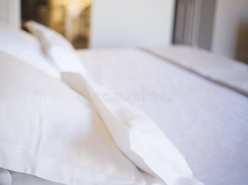 Luxury hotel bedroom bed clean ironed tidy cotton sheets and pillows ready for guests to sleep.