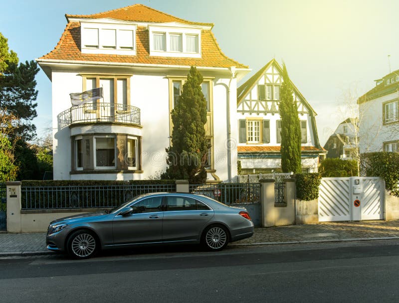 Luxury Mercedez-Benz S Class limousine parked in front of traditional Alsatian house