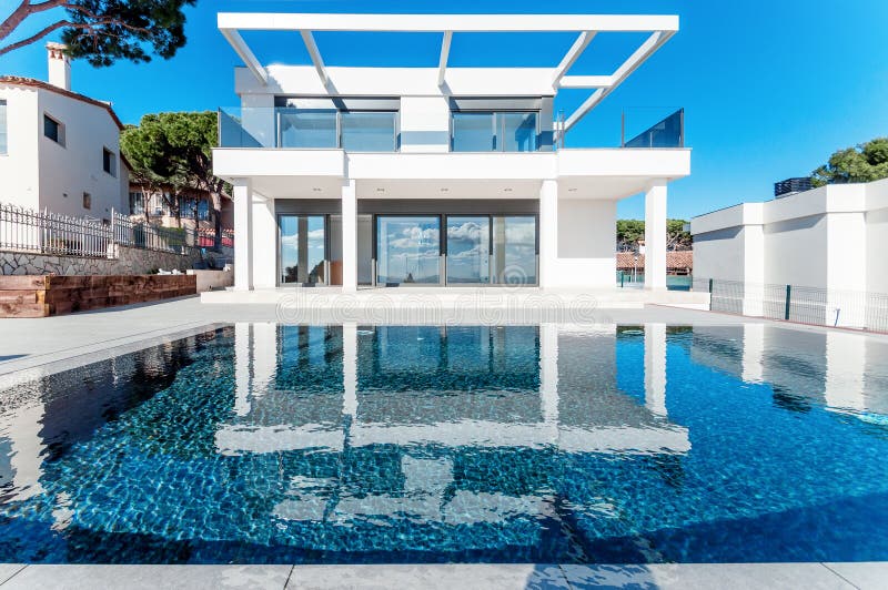 Luxury modern white house with large windows overlooking a Mediterian landscaped garden with palm trees and  blue swimming pool.