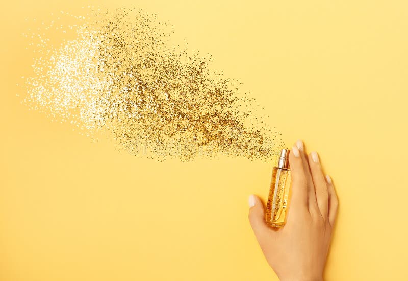 Luxury perfume concept. Female hand holding stylish bottle of perfume with spray of sparkles on yellow background stock photography Luxury perfume concept. Female hand holding stylish bottle of perfume with spray of sparkles on yellow background stock photography