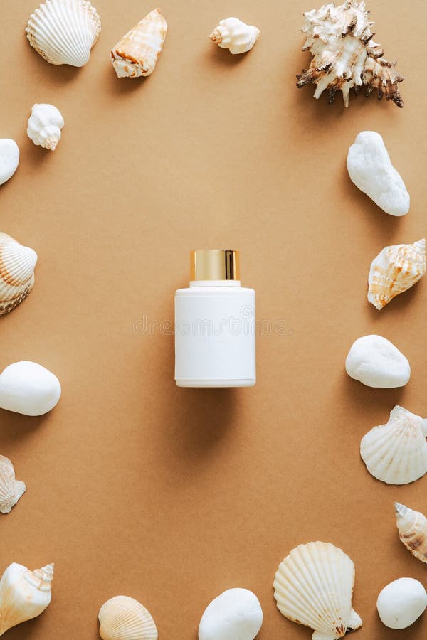 Luxury sunscreen lotion bottle and frame of seashells on sand colored background. Flat lay, top view, copy space. Beauty product