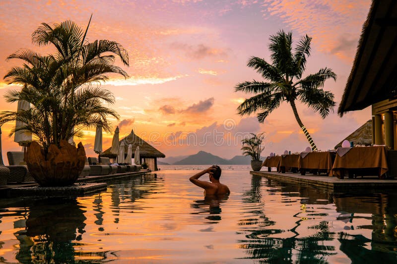 Luxury swimming pool in tropical resort, relaxing holidays in Seychelles islands. La Digue, Young man during sunset by