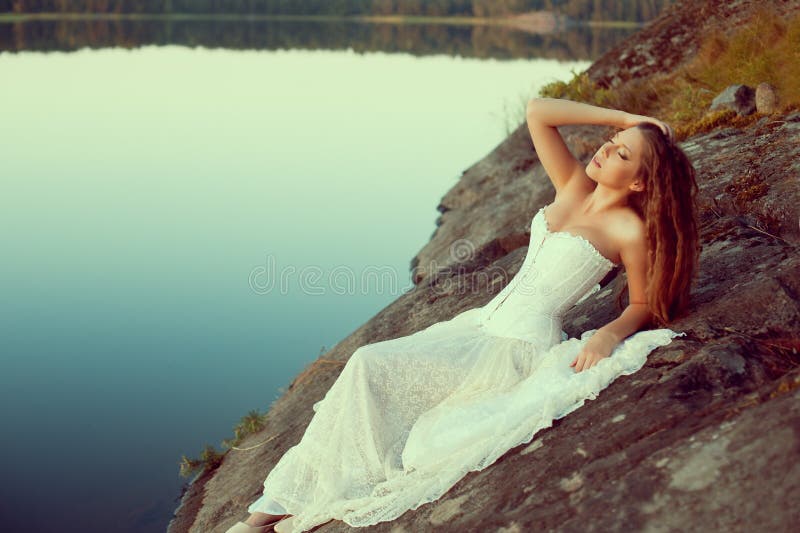 Luxury woman in a forest in a long vintage dress near the lake.