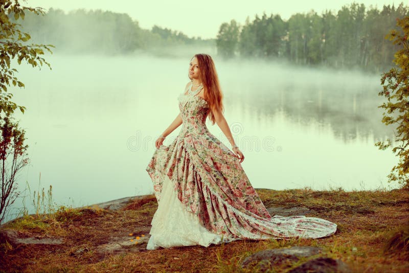 Luxury woman in a forest in a long vintage dress near the lake.