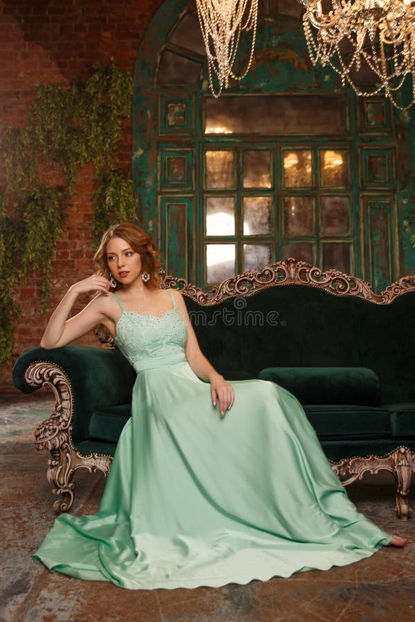 Luxusfrauenmodell in einem Minze-farbigen Kleid, das auf einer Weinlesecouch sitzt Schönheitsmädchen mit einem erstaunlichen Make stockbild