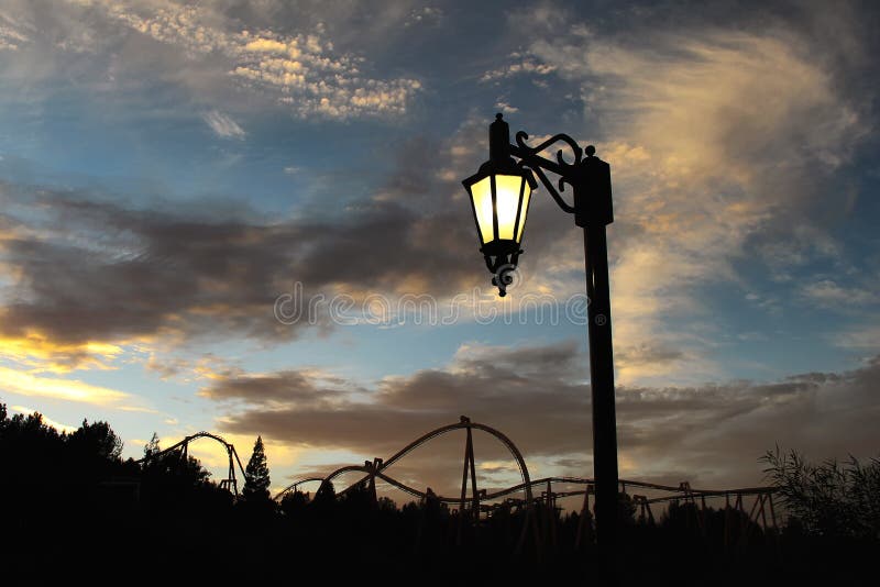 Luz de calle y una silueta de la montaña rusa en el fondo imagen de archivo libre de regalías Luz de calle y una silueta de la montaña rusa en el fondo imagen de archivo libre de regalías