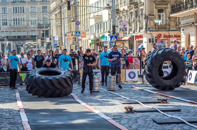 LVIV, UCRANIA - JUNIO DE 2016: Un hombre fuerte en el culturista de la forma de los deportes aumenta la rueda pesada en la calle foto de archivo libre de regalías LVIV, UCRANIA - JUNIO DE 2016: Un hombre fuerte en el culturista de la forma de los deportes aumenta la rueda pesada en la calle foto de archivo libre de regalías