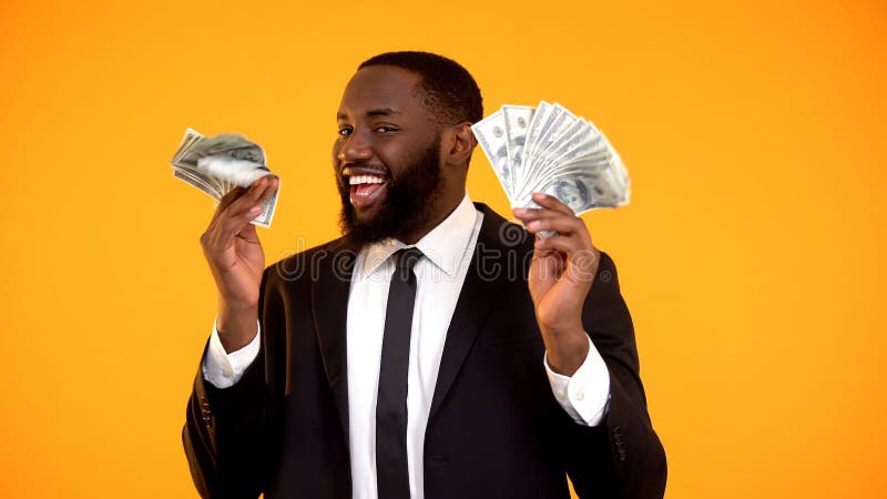 Lyckad svart man i aff?rsdr?kten som rymmer grupper av kassa och att le f?r dollar royaltyfria foton Lyckad svart man i aff?rsdr?kten som rymmer grupper av kassa och att le f?r dollar royaltyfria foton