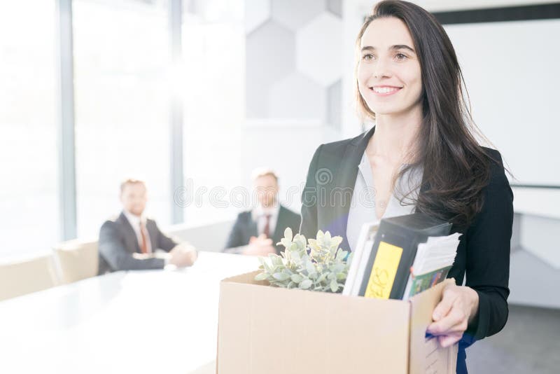 Waist up portrait of happy young businesswoman holding box of personal belongings leaving office after quitting job, copy space. Waist up portrait of happy young businesswoman holding box of personal belongings leaving office after quitting job, copy space