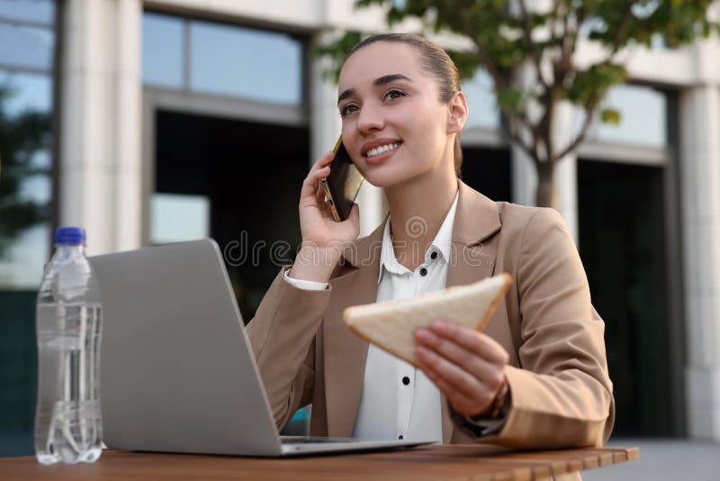 Lycklig affärsman med smörgåspålägg på smartphone under lunch på träbord utomhus arkivfoton
