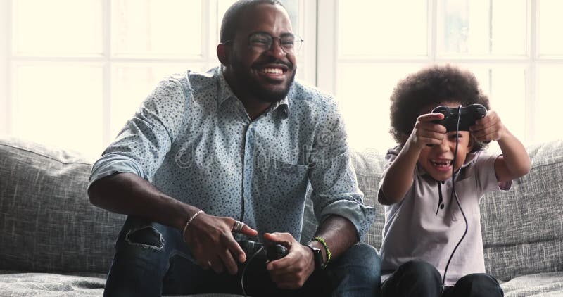 Lycklig afrikansk amerikansk pappa spelar videospel med liten son. arkivfilmer