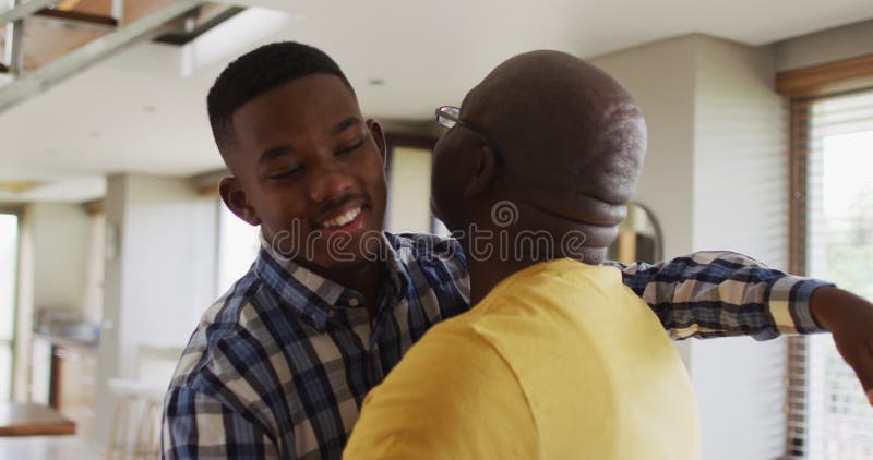 Lycklig afrikansk amerikansk äldre far som omfamnar sin tonåriga son och leende