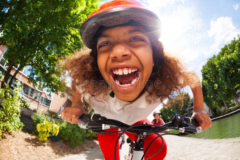 Close-up portrait of smiling African girl in safety helmet riding her bicycle at sunny day in full speed. Close-up portrait of smiling African girl in safety helmet riding her bicycle at sunny day in full speed