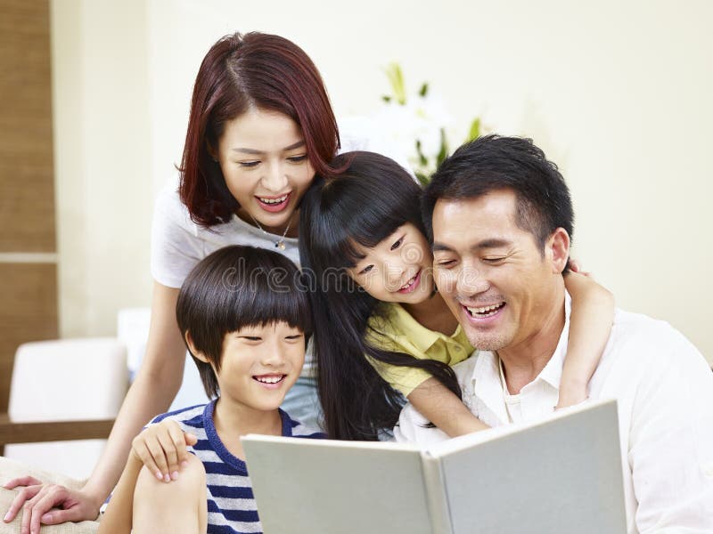 Lycklig asiatisk familj som hemma läser en bok arkivbild