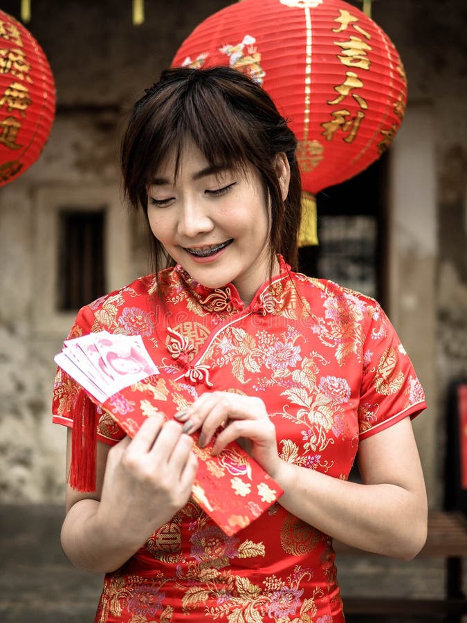 Lycklig asiatisk kvinna i den traditionella kinesiska klänningen som rymmer ett rött fack med kinesiska hundra lyckliga pengar fö arkivbilder Lycklig asiatisk kvinna i den traditionella kinesiska klänningen som rymmer ett rött fack med kinesiska hundra lyckliga pengar fö arkivbilder