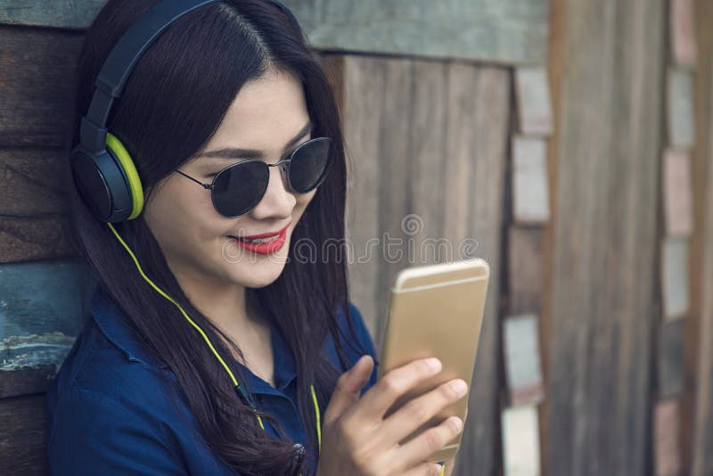 Lycklig asiatisk kvinna som lyssnar till musik på hennes headphone och watchi arkivbild Lycklig asiatisk kvinna som lyssnar till musik på hennes headphone och watchi arkivbild