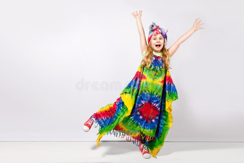 Lycklig blond barnflicka i färgrik klänning för hippie mot den vita väggen fotografering för bildbyråer Lycklig blond barnflicka i färgrik klänning för hippie mot den vita väggen fotografering för bildbyråer