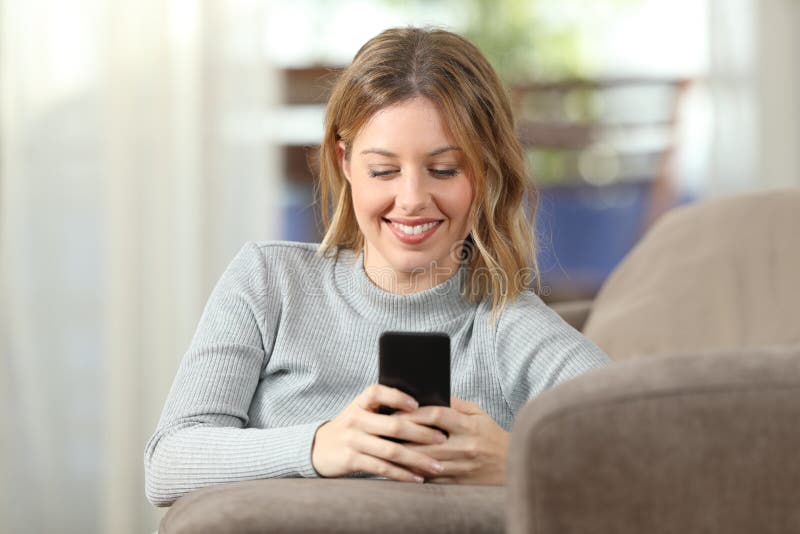 Lycklig dam som hemma smsar på telefonen på en soffa royaltyfria bilder Lycklig dam som hemma smsar på telefonen på en soffa royaltyfria bilder