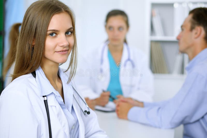 Lycklig doktorskvinna med den medicinska personalen på bakgrunden i sjukhuskontor royaltyfria foton Lycklig doktorskvinna med den medicinska personalen på bakgrunden i sjukhuskontor royaltyfria foton