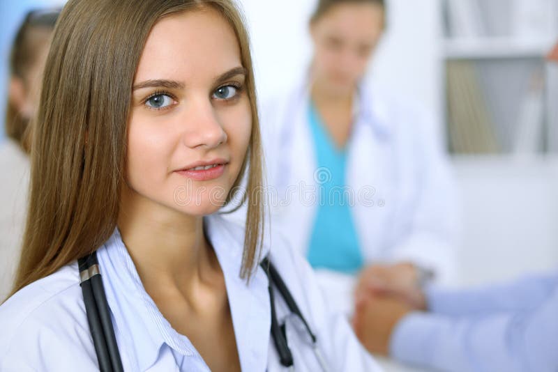 Lycklig doktorskvinna med den medicinska personalen på bakgrunden i sjukhuskontor arkivfoton Lycklig doktorskvinna med den medicinska personalen på bakgrunden i sjukhuskontor arkivfoton