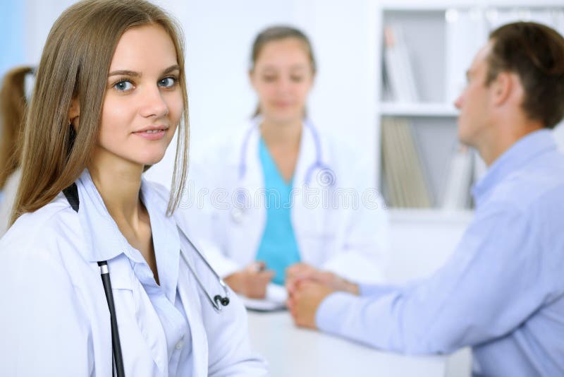 Lycklig doktorskvinna med den medicinska personalen på bakgrunden i sjukhuskontor arkivfoto Lycklig doktorskvinna med den medicinska personalen på bakgrunden i sjukhuskontor arkivfoto