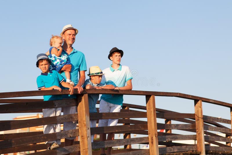 Lycklig fader med hans söner och litet dotteranseende på träbron royaltyfria foton Lycklig fader med hans söner och litet dotteranseende på träbron royaltyfria foton