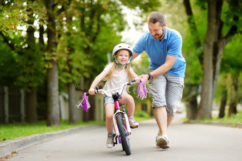Lycklig fader som undervisar hans lilla dotter att rida en cykel Barn som lär att rida en cykel arkivbilder