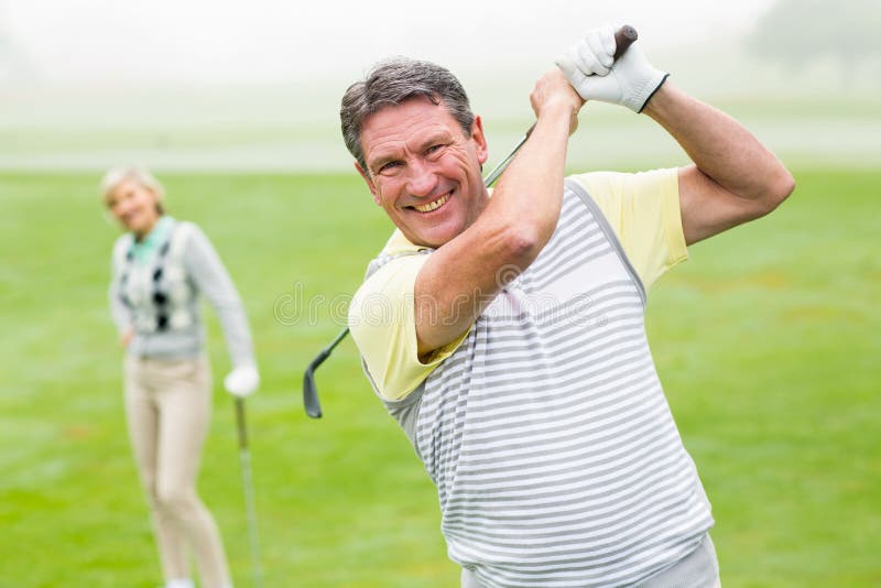Lycklig golfare som teeing av med partnern bak honom royaltyfri foto Lycklig golfare som teeing av med partnern bak honom royaltyfri foto