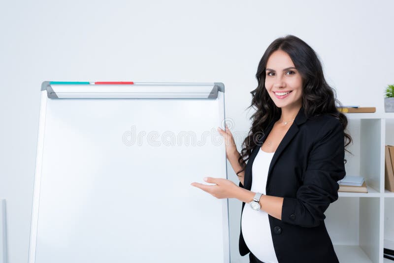 lycklig gravid affärskvinna som pekar på den tomma whiteboarden och att se royaltyfri fotografi lycklig gravid affärskvinna som pekar på den tomma whiteboarden och att se royaltyfri fotografi
