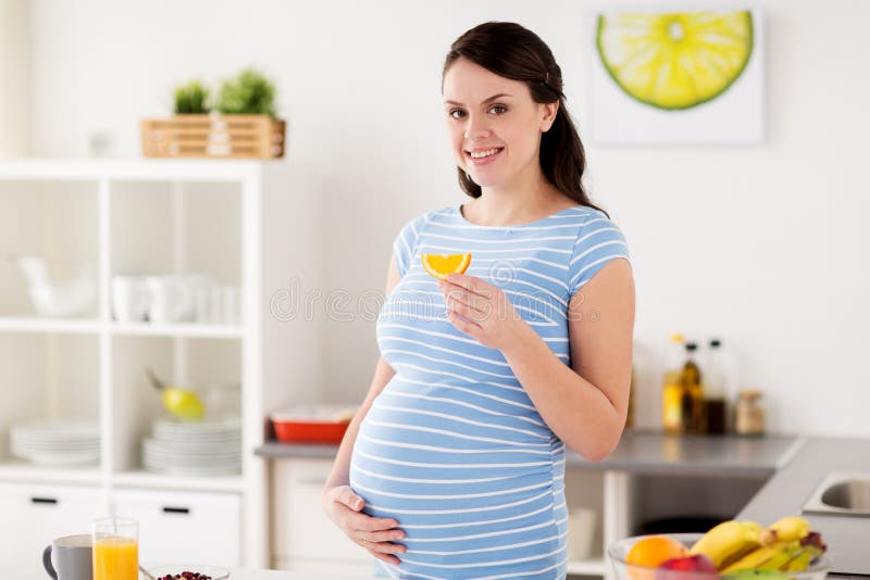 Lycklig gravid kvinna som äter orange hemmastatt