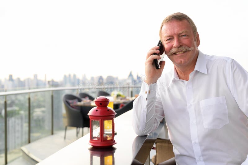 Lycklig hög affärsman som ler, medan kalla med telefonen på takrestaurangen arkivbild Lycklig hög affärsman som ler, medan kalla med telefonen på takrestaurangen arkivbild