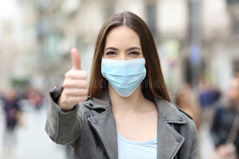 Front view portrait of a happy woman with protective mask gesturing thumbs up in the street. Front view portrait of a happy woman with protective mask gesturing thumbs up in the street
