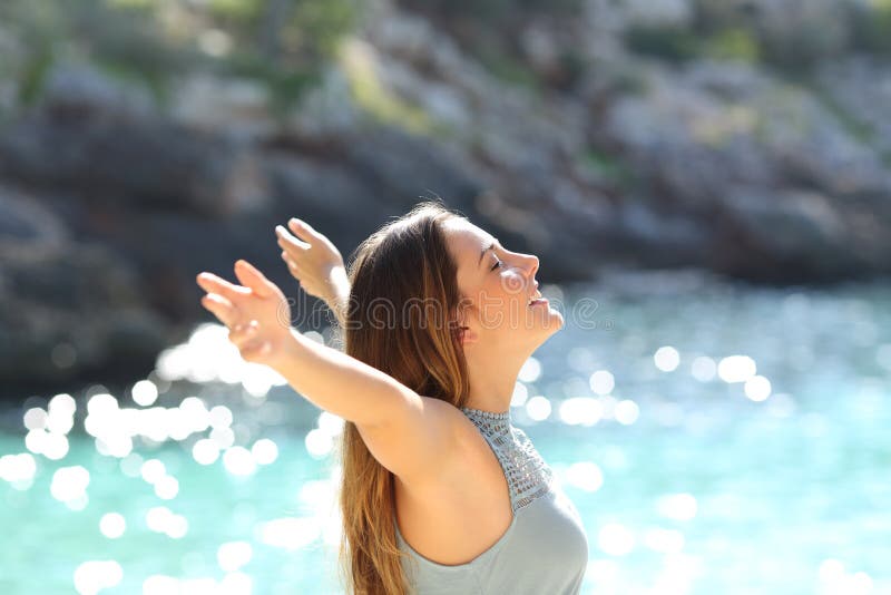 Lycklig kvinna som andas ny luft som lyfter armar på ferier