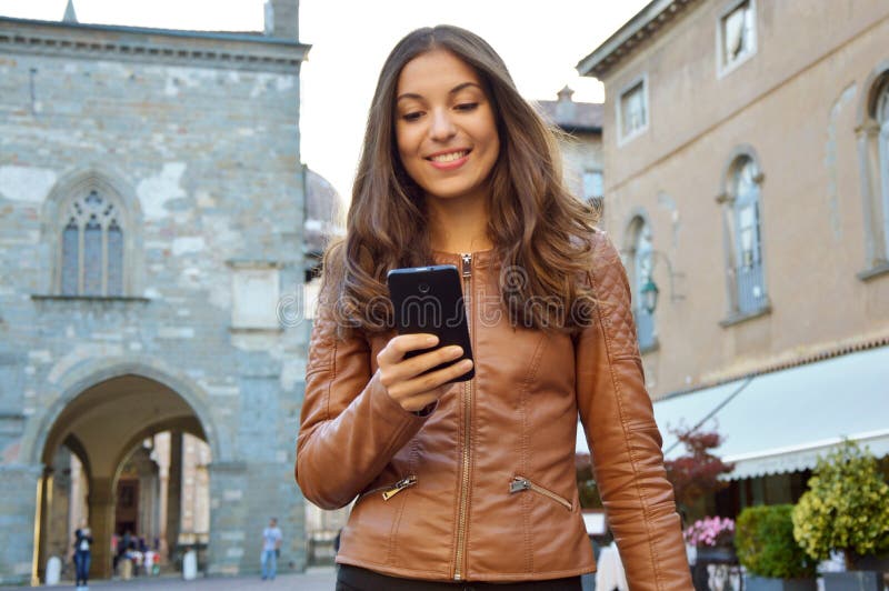 Lycklig kvinna som ler och går i gatan genom att använda en ny app på smartphonen arkivbild Lycklig kvinna som ler och går i gatan genom att använda en ny app på smartphonen arkivbild