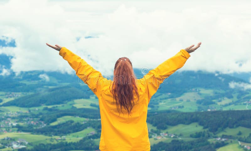 Lycklig kvinna som står upp med armar som höjs vid bergstoppen
