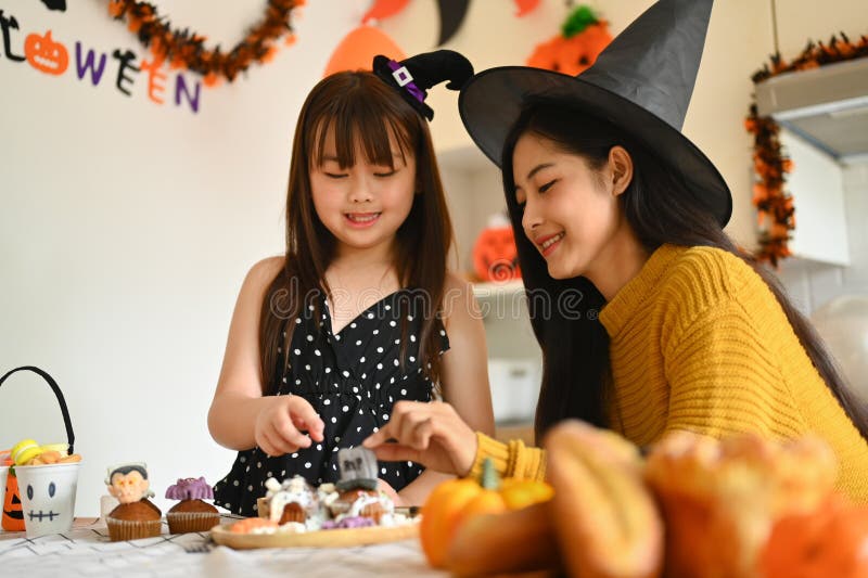 Lycklig liten flicka och mor som dekorerar halloween cupcakes med olika monster på köksbordet royaltyfri bild