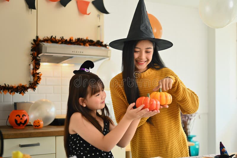 Lycklig liten flicka och mor som håller pumpor medan de förbereder sig för halloween i köket arkivbilder
