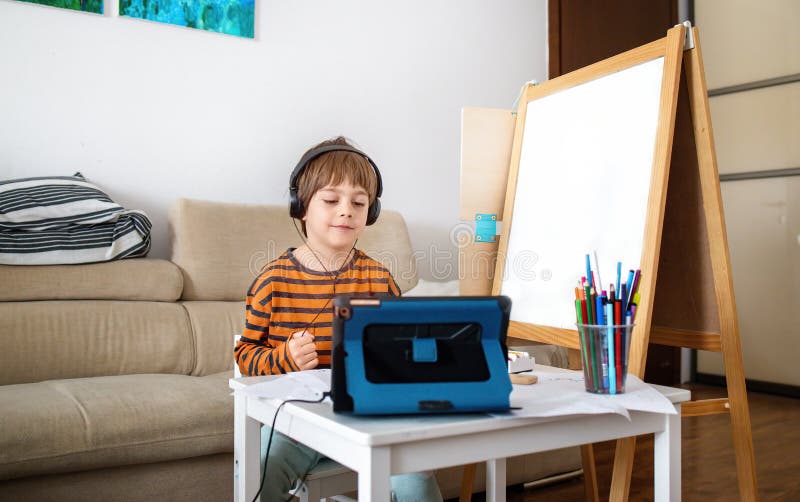 Lycklig liten pojke som går i onlinekurser från hemmet. barn som använder digitala surfplattor och headset för att ansluta till lä arkivbilder